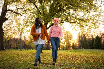 Obraz premium Diverse women friends holding hands walking in autumn park