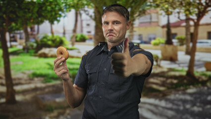 Man police officer smiling and holding donut with outstretched hand, badge visible on uniform, standing on street; playful camaraderie.