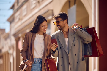 Happy couple using cell phone while shopping in the city.