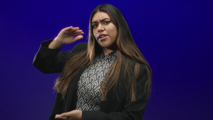 Woman holds pinched fingers and hands spaced as if measuring a small object in a studio with a deep blue backdrop; skepticism.