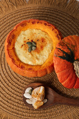 Pumpkin filled with creamy dish next to a whole pumpkin and seeds on a woven mat