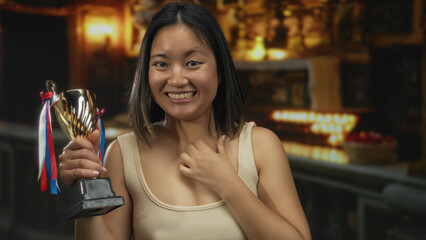 Chinese woman holding trophy smiling inside a warmly lit church with candles and religious decor highlighting her joyful expression and achievement.