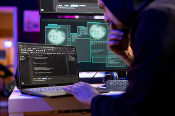 Hacker in secret lair coding on laptop to break into secure computer systems and bypass security. Rogue engineer uses programming languages on notebook to attack weak spots in company networks