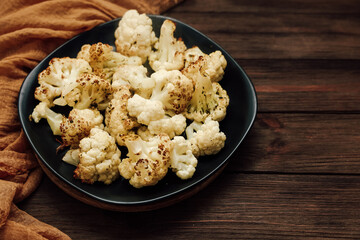 Oven roasted cauliflower pieces on a black plate with a brown cloth on a wooden table