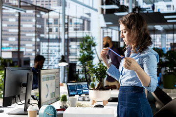 Enthusiastic woman on her first day at new job unpacking things at her workstation, feeling excited and hopeful about joining the team within the corporation. Newcomer unboxing belongings.