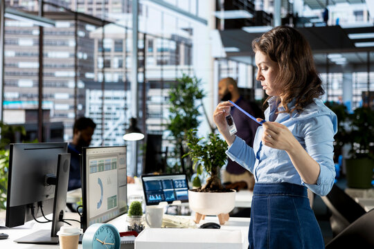 Enthusiastic woman on her first day at new job unpacking things at her workstation, feeling excited and hopeful about joining the team within the corporation. Newcomer unboxing belongings.