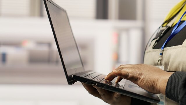 Technician in sustainable industrial plant monitors production equipment using laptop, diagnosing malfunctions. Factory worker coordinates repair tasks on solar module assembly line, camera B close up