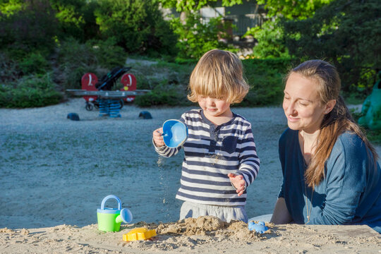 Mother and cute little child boy having fun playing with sand and colorful toys in the park, beautiful summer sunny day in children playground. Selective focus