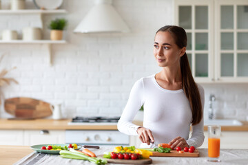 Woman in the kitchen preparing nourishing meals by chopping fresh vegetables, adhering to the principles of balanced diet.