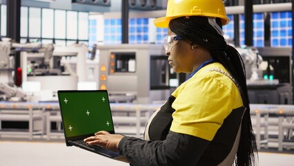 Factory engineer typing on green screen laptop, monitoring production lines. Woman in industry 4.0 plant ensures machinery operates at optimal efficiency using chroma key mockup notebook, camera A