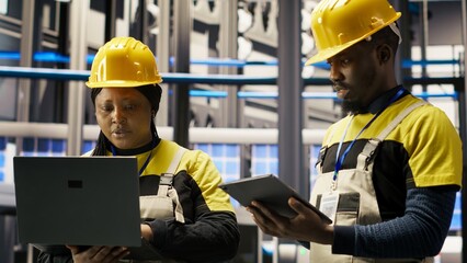 Team of smart factory mechanics working together to test systems, doing maintenance. Industry 4.0 plant teamworking repairmen inspecting equipment to identify glitches, doing brainstorming, camera B
