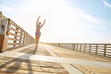 Outdoor, travel and celebration with happy woman on vacation, freedom or adventure with mockup space. Holiday, hands up and person walk for summer trip, tourism and getaway on walkway with sunshine