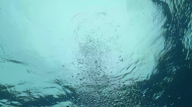 Air bubbles rise vertically toward the surface in deep blue ocean water, seen from below like a drowning point of view, creating tension, motion, and abstract underwater drama.