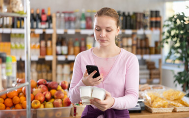 Checking expiration date of yogurt - female shopper scans QR code on label of yogurt using her smartphone