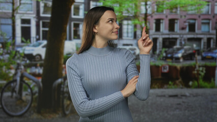 Woman pointing finger upward on a city street with canal buildings and bicycle; confidence inspiration.