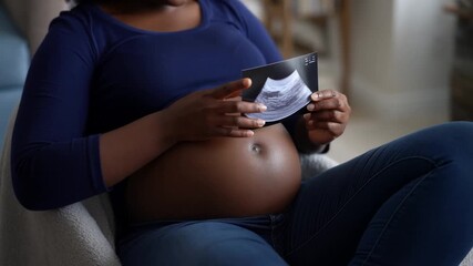 A pregnant woman happily looking at an ultrasound image, anticipating motherhood. The woman is seated comfortably in a chair, with a look of joy and anticipation Stock Video