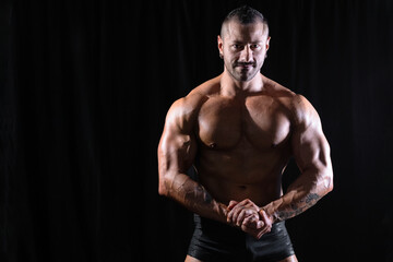 Fototapeta premium Strong male bodybuilder posing in front view on a black background, emphasizing defined chest, arms, and upper body structure. Studio lighting enhances muscle definition, power, and the aesthetics of 
