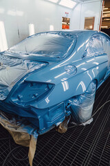 Professional car painting in a specialized spray booth at an auto service center. Body repair and surface preparation process. Quality maintenance and technical service for modern vehicle transport.