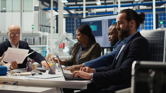 Factory engineering team using laptop to refine designs for increased energy output using collected data. Photovoltaics plant specialists design innovative solar cell prototypes on notebook, camera A