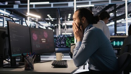 Engineer in data center frustrated by critical error popup on monitor during diagnostics session. IT expert stressed while troubleshooting system fault affecting infrastructure performance, camera A
