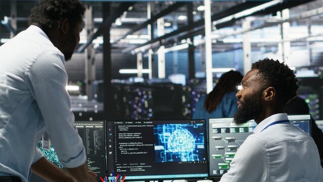 Server hub manager checking AI generated data analytics graphs, congratulating worker. Data center team leader doing fist bump with admin using artificial intelligence showing system metrics, camera B
