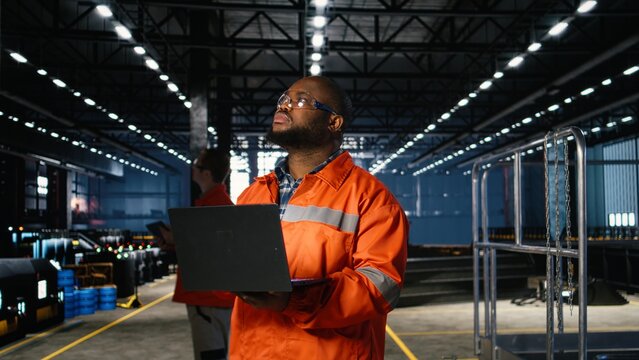 African american technician in protective gear oversees welding equipment next to sparks on factory floor, reflecting heavy labor and the automation development of the industry plant.