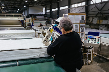 Worker sewing edges of mattress with sewing machine