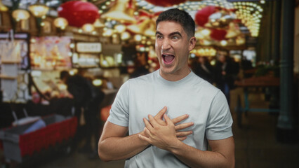 Obraz premium Man smiling with open mouth and hands on stomach in street market with hanging lights and souvenir stalls; joy.