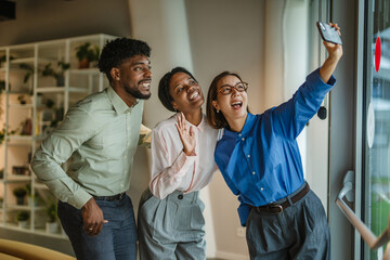 Diverse friends taking office selfie bonding and laughing