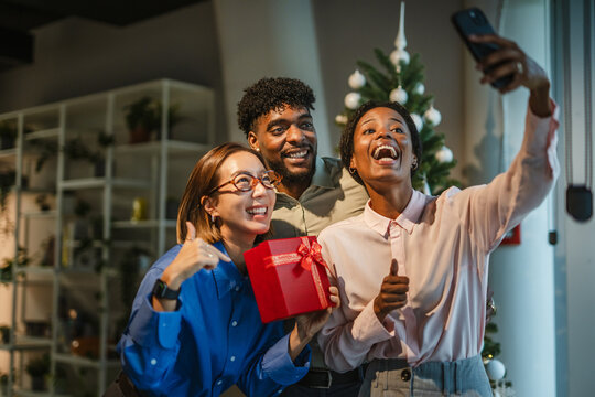 Diverse friends taking selfie celebrating office christmas party with gift - Powered by Adobe