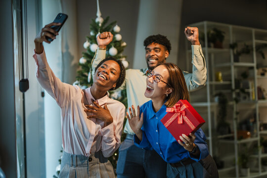 Diverse friends taking selfie celebrating office christmas party with gift