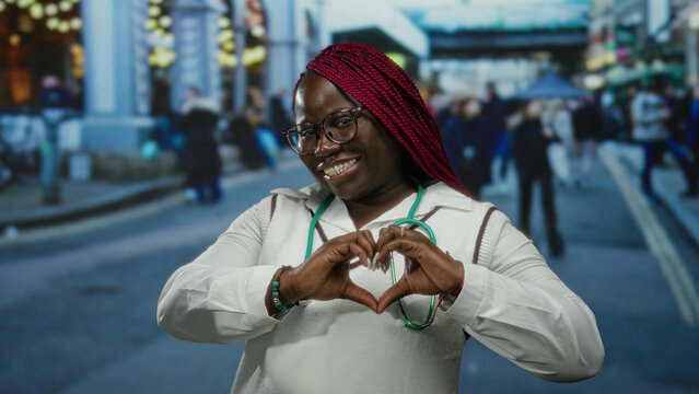 Woman smiling with red braids forms heart shape with hands in bustling city street setting showcasing joy friendliness and urban lifestyle. - Powered by Adobe