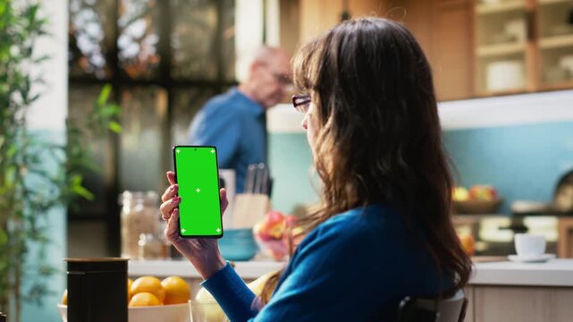 Mockup display on phone at kitchen table with elderly woman smiling and relaxing, serving coffee and meal for breakfast at the table. Fun retirement lifestyle from comfortable rustic home. Camera B.