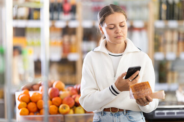 Female shopper scans the barcode on a cheese package. Grocery store visitor uses an online application on her mobile to pay
