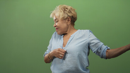 Senior hispanic woman wearing a blue blouse and bracelets gestures with hand to chest while extending her arm in a studio; joyful motion.