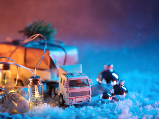 A toy truck is transporting a Christmas gift, a snowy festive background with a garland and balloons. Delivery concept