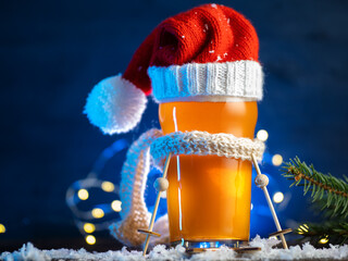 Christmas beer glass in a knitted Santa Claus hat and scarf. Blue background with copy space