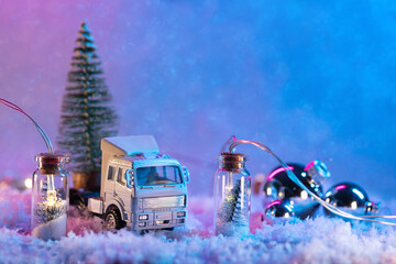 A toy truck is carrying a Christmas tree, a snow background with a garland and balloons. Copy space