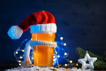 Christmas beer glass in a knitted Santa Claus hat and scarf. Blue background with copy space