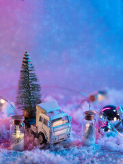 Festive New Year's card, toy truck transporting a Christmas tree in the back on a snowy background , colored light, copy space