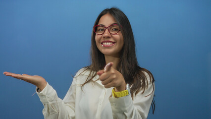 Young hispanic woman smiling and pointing at her left hand presenting something against an isolated...