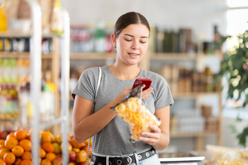 Young woman buyer scanning qr code for crispy snack mix in grocery store