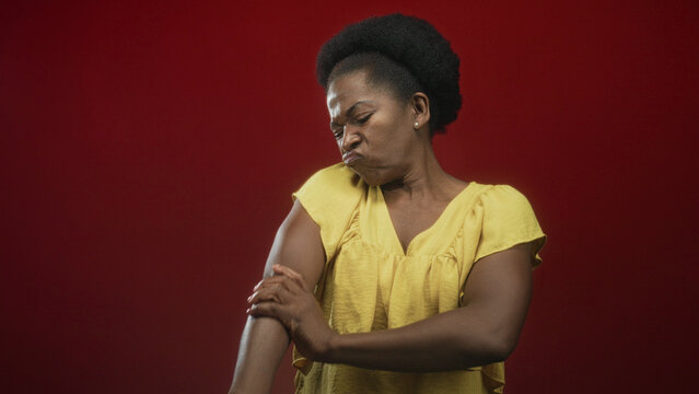 Woman rubbing her forearm and inspecting her arm in a studio with a red backdrop; discomfort reflection.