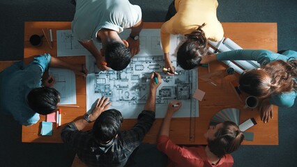 Top down view of civil engineer team writing at blueprint at meeting table with color palettes. Group of diverse people planning and taking a note while manager looking at project plans. Symposium.