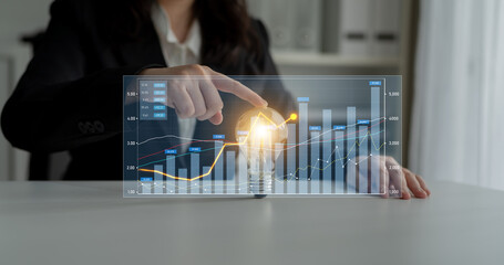 A business professional engages with a digital financial graph and a light bulb, symbolizing innovative thinking and strategic analysis in a modern office setting. Scalp