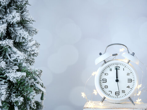 New Year’s midnight clock and twinkle fairy lights with winter snow on spruce pine tree on a blurry gray backdrop. Celebration for the new year. - Powered by Adobe
