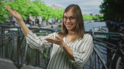 Woman extends hands to side on a street beside an amsterdam canal, smiling and gesturing palm up; joy welcome.