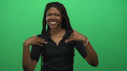 Woman smiling and pointing both index fingers while offering open hands in studio with bright green backdrop; joyful welcome.