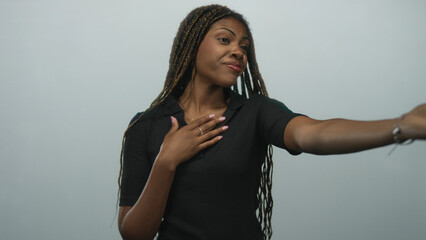 Woman with hands on chest smiling in studio against a soft light gray backdrop, reaching outward in an open pose; gratitude warmth appreciation.