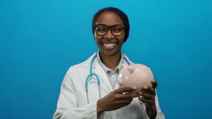 Woman smiling with piggy bank in blue background wearing doctor coat and stethoscope, symbolizing medical savings concept.